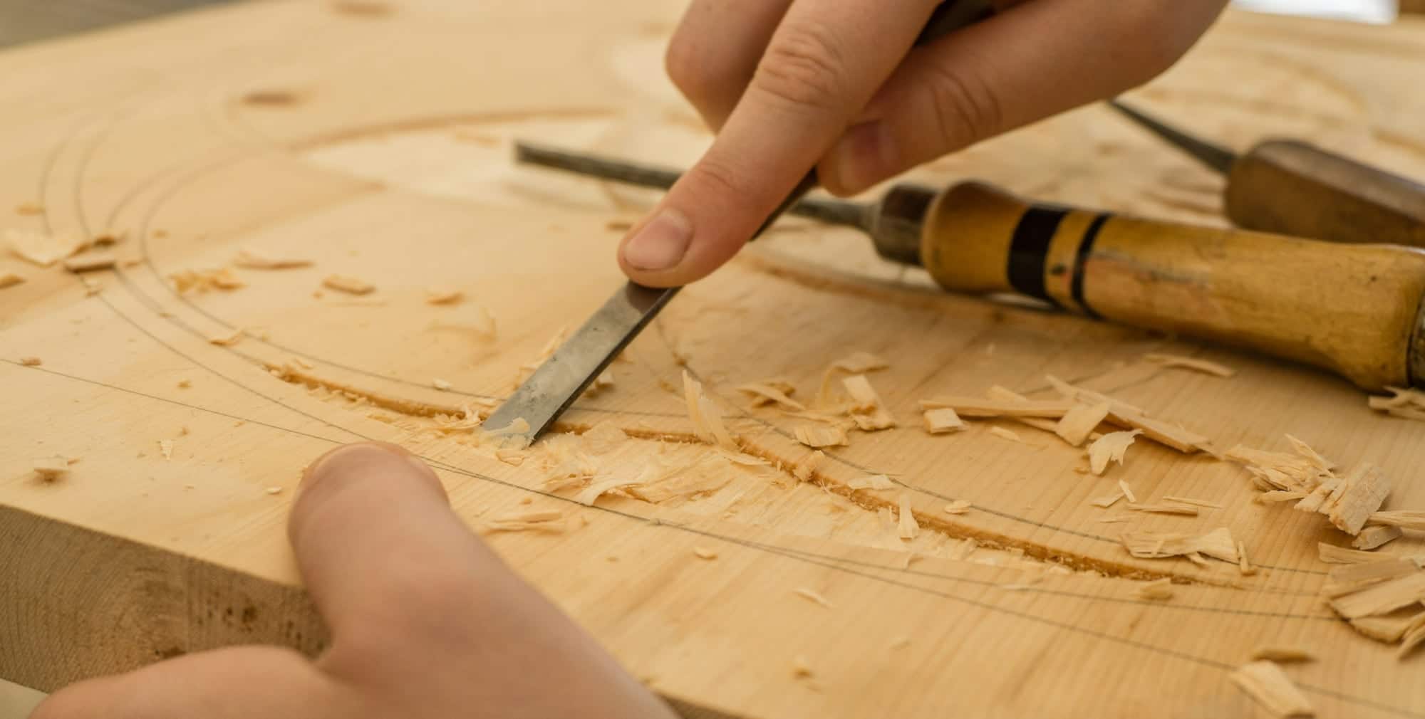 Mains d'un artisan creusant une planche de bois clair au ciseau à bois, au milieu des copeaux