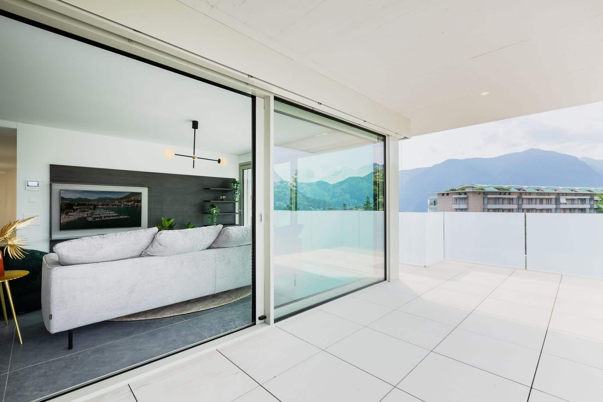 Grande baie vitrée coulissante à cadre fin, ouverte entre un salon contemporain et une terrasse carrelée
